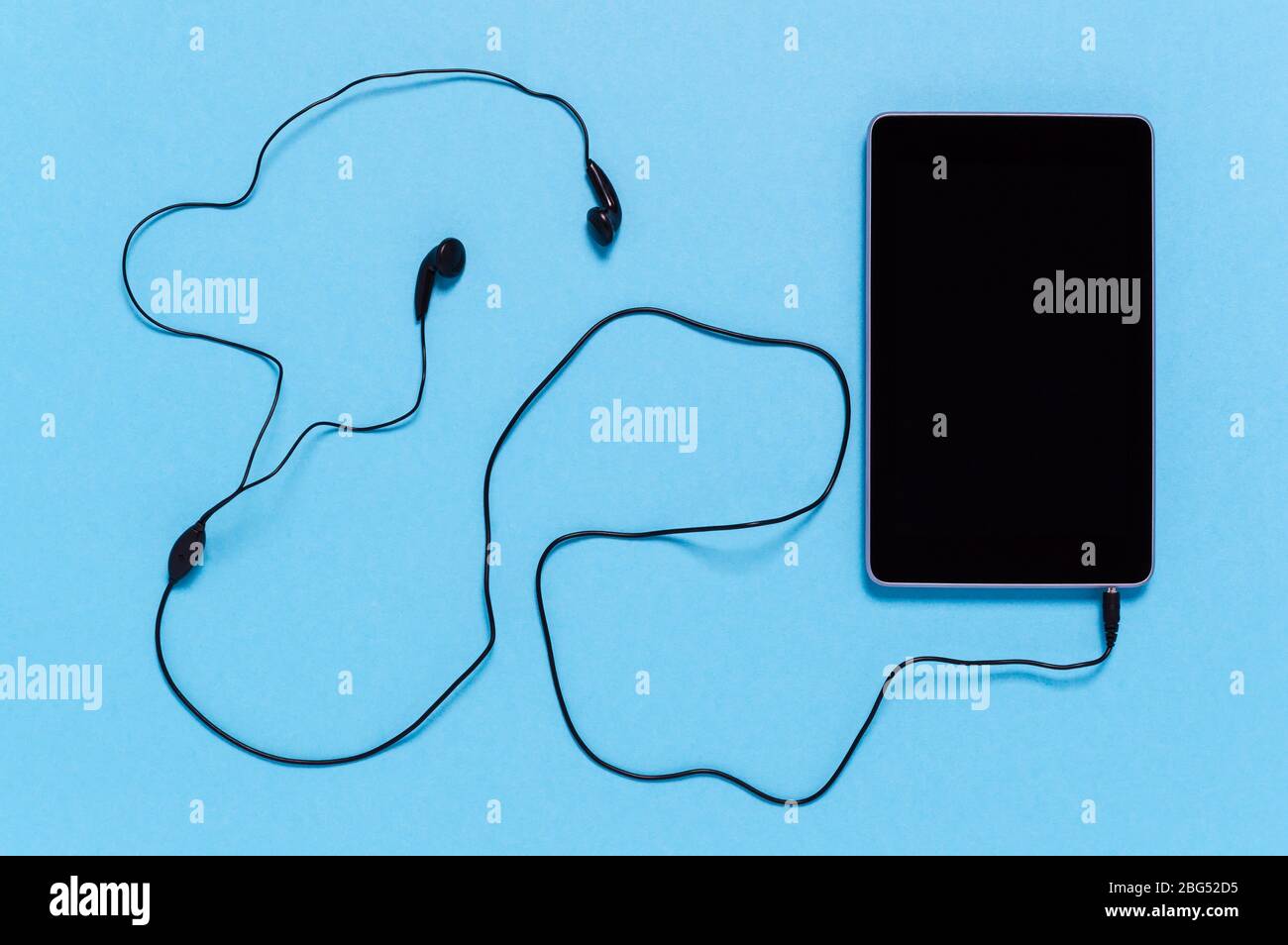 Tablet nero con auricolari su sfondo blu. Concetto minimo di connettività, lavoro digitale remoto o intrattenimento multimediale come lo streaming musicale Foto Stock