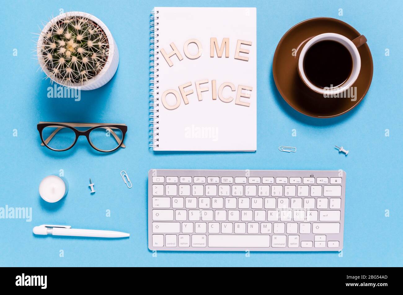 Piatto di spazio di lavoro moderno con tastiera, tazza da caffè, blocco note, penna, occhiali e cactus su sfondo blu. Lettere che dicono Ufficio domestico. Vista dall'alto Foto Stock