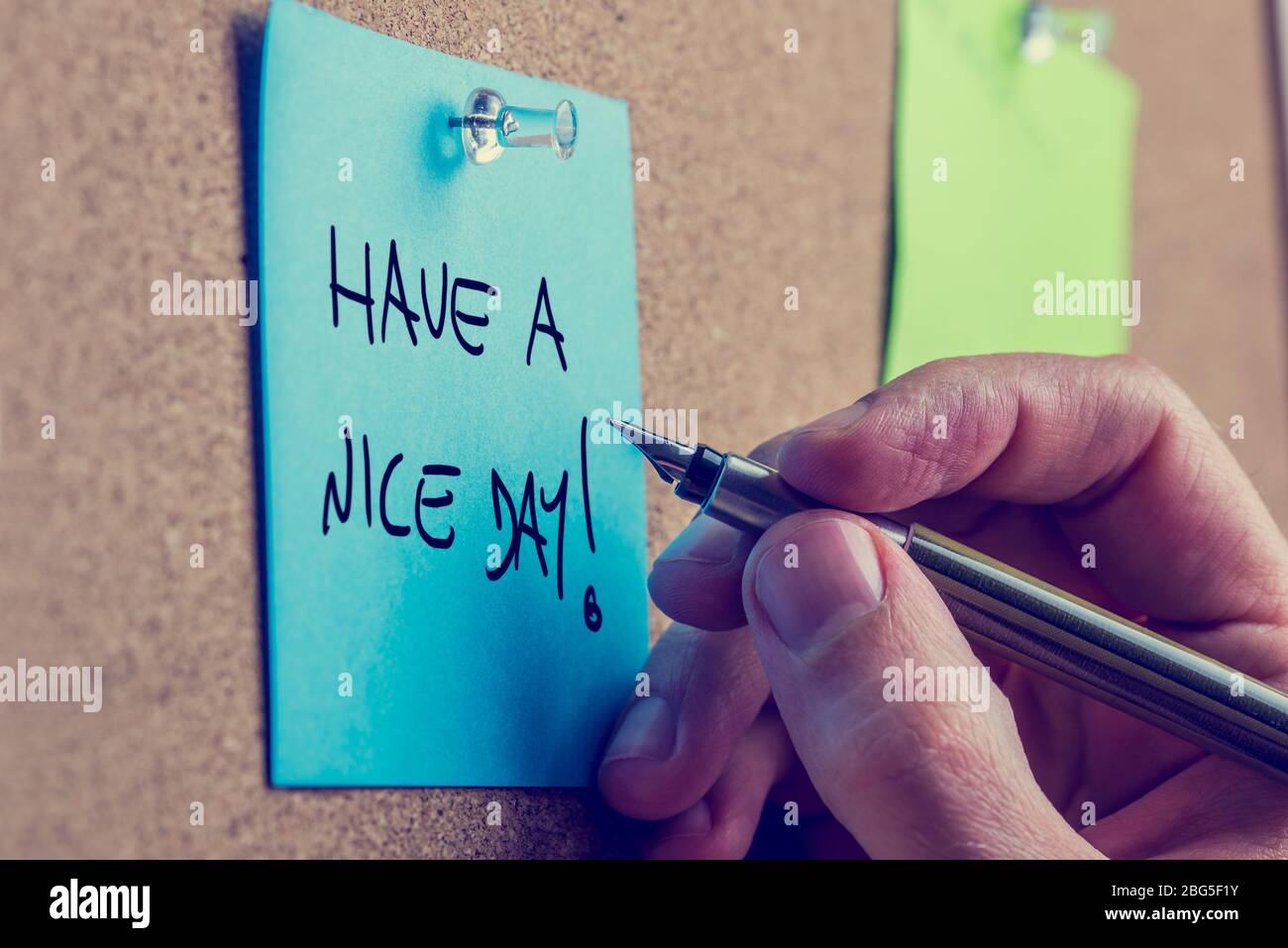 Closeup di scrittura mano maschio hanno un messaggio di giorno piacevole su un post blu carta pinned ad un bordo del bollettino del sughero, toned retro o effetto instagram. Foto Stock