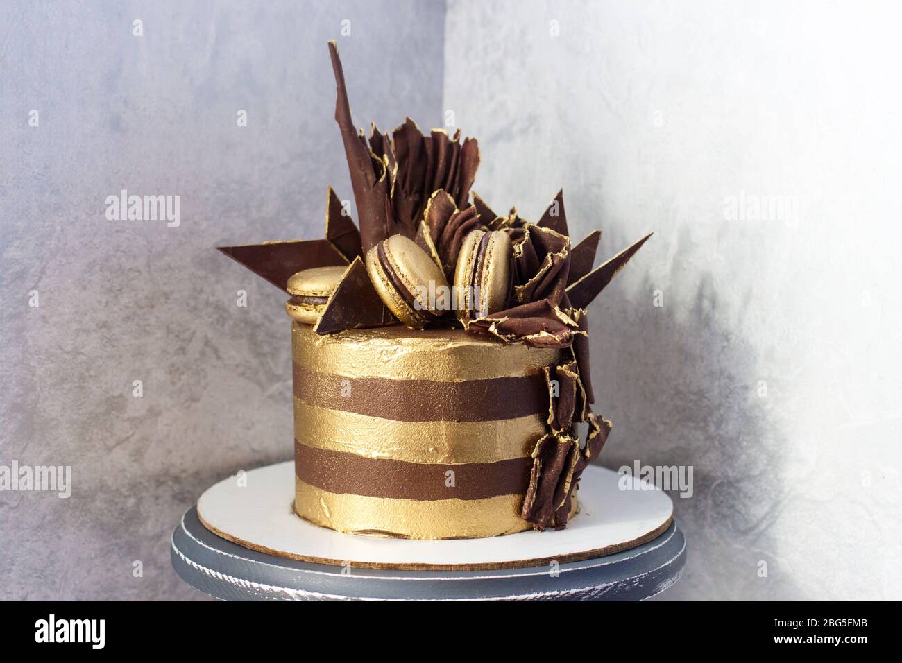 Torta di compleanno al cioccolato con strisce dorate, decorazione al cioccolato fondente e macaroon. Foto Stock
