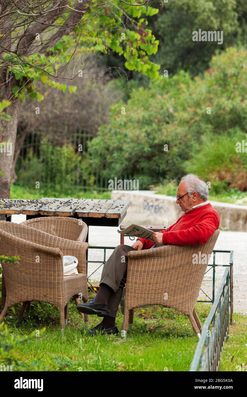 Un uomo solo che legge il giornale in via Apostolou Pavlou, distretto di Thisio, durante il blocco ufficiale dovuto lo scoppio del coronavirus in Grecia. Foto Stock