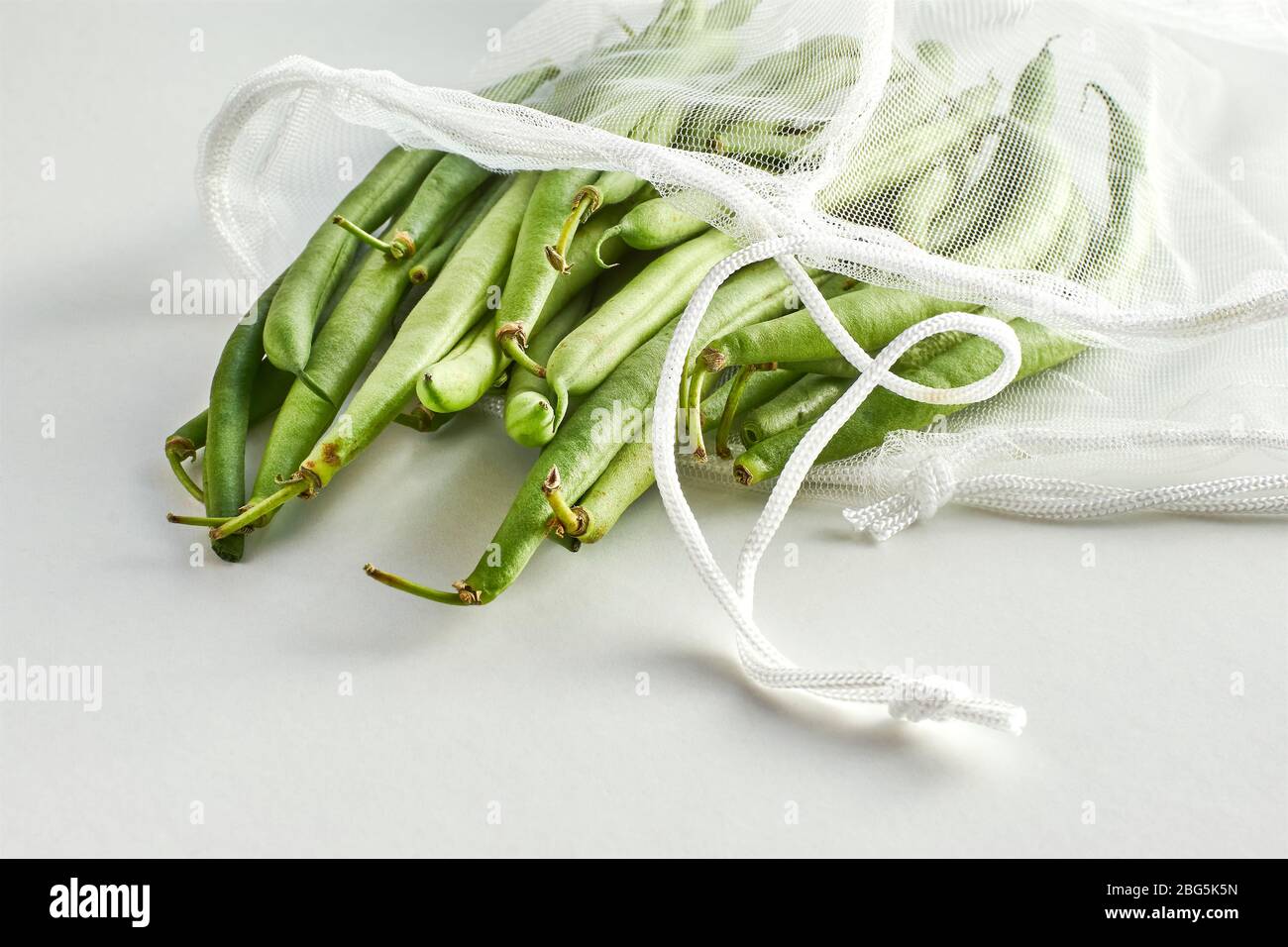 Fagioli verdi in una borsa a rete di prodotti alimentari sostenibile. Verdure in imballaggi riutilizzabili ecologici su sfondo chiaro. Zero sprechi shopping, senza plastica. Foto Stock