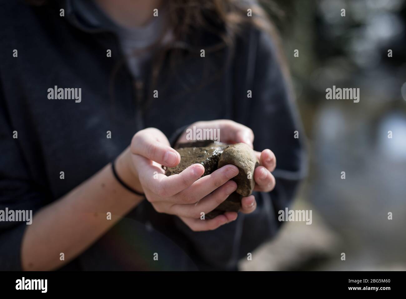 Una ragazza dai capelli marroni, con un pullover grigio con zip 3/4, un pelo che rotola attorno al polso, tenendo le rocce bagnate, raccolte da Pitville Park. Foto Stock