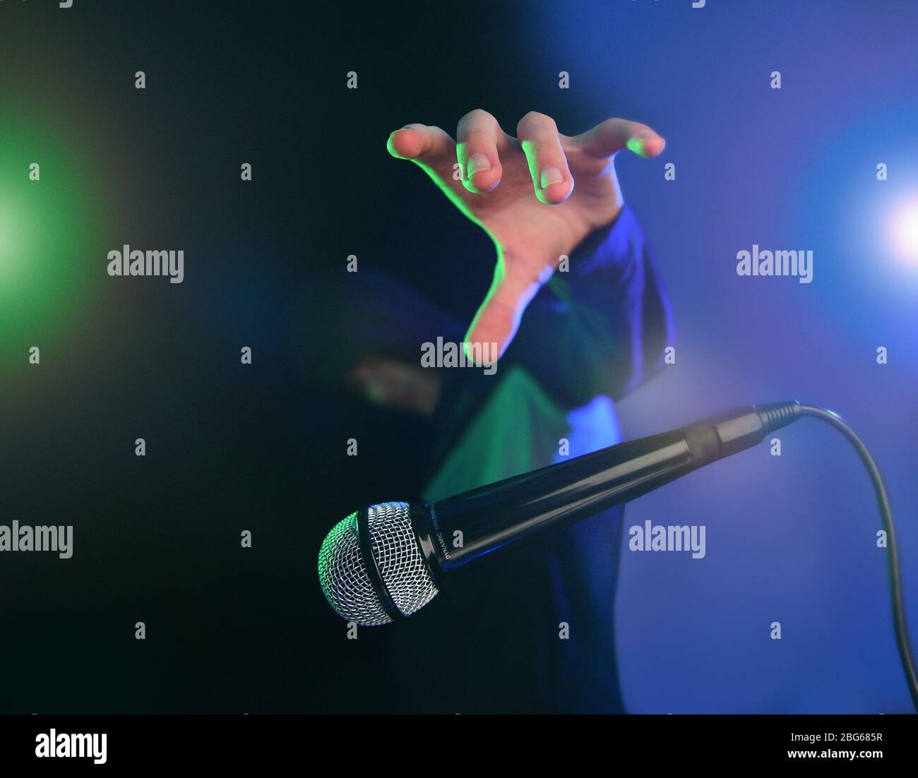Rilasciare l'immagine del concetto del microfono. Scatto con illuminazione da palco effetto multicolore e cool dude con una felpa con cappuccio. Foto Stock