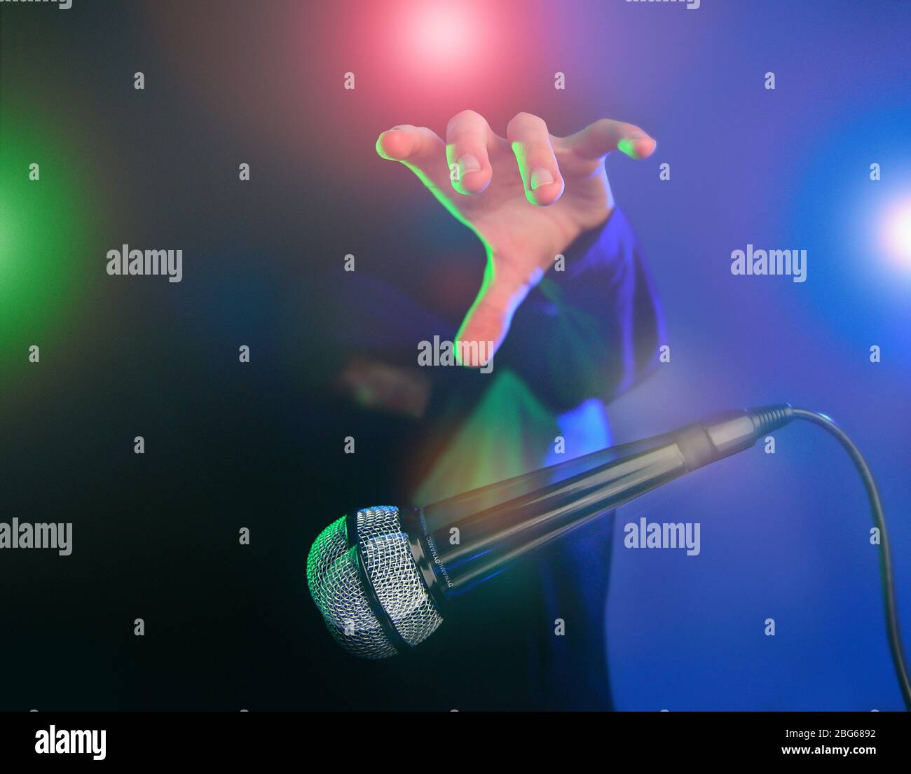 Rilasciare l'immagine del concetto del microfono. Scatto con illuminazione da palco effetto multicolore e cool dude con una felpa con cappuccio. Foto Stock