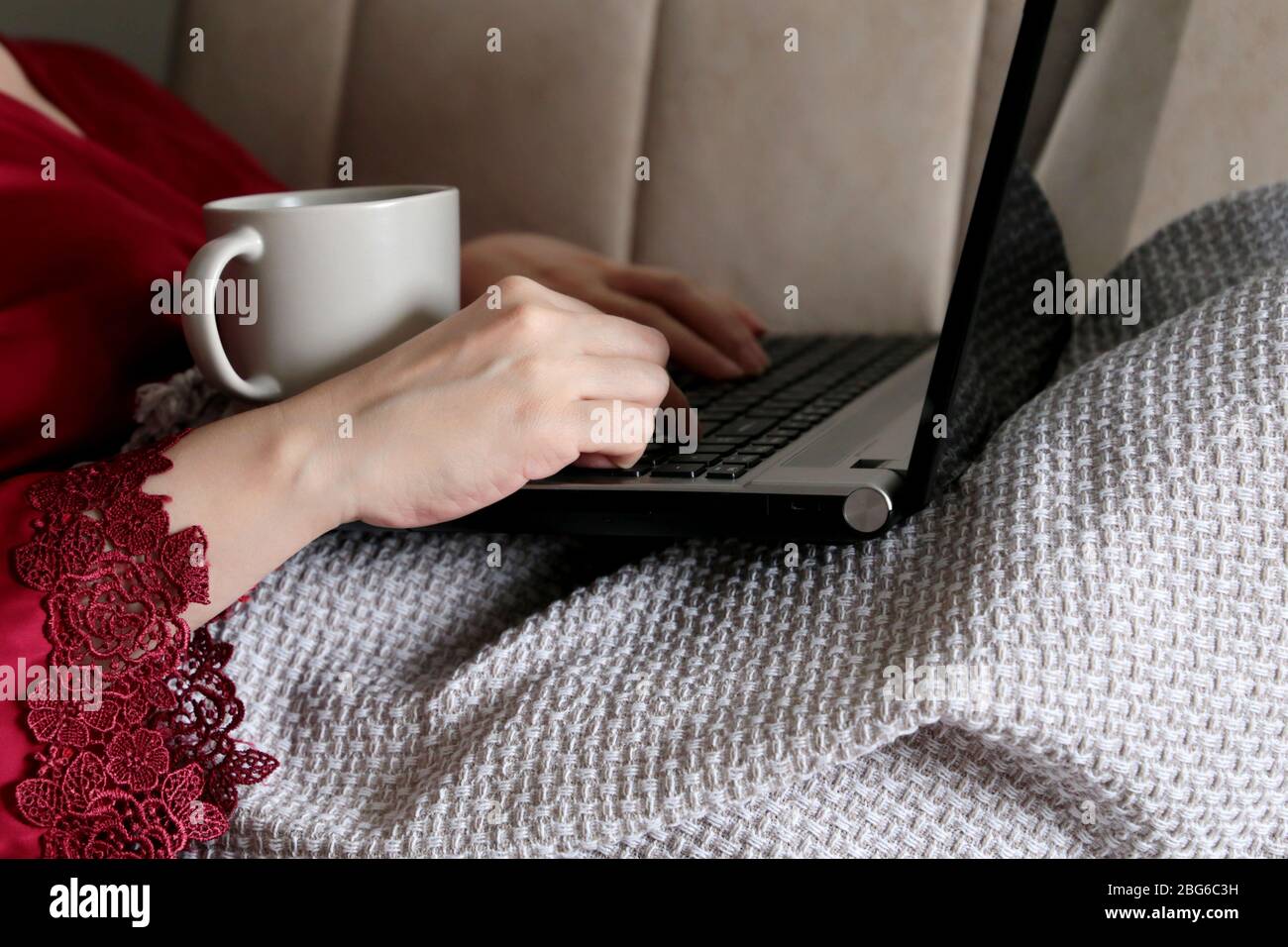 Donna coperta con una plaid utilizzando il laptop, lavoro a distanza durante la quarantena a casa. Ragazza con tazza di bevanda calda, concetto di lavoro durante il covid-19 Foto Stock