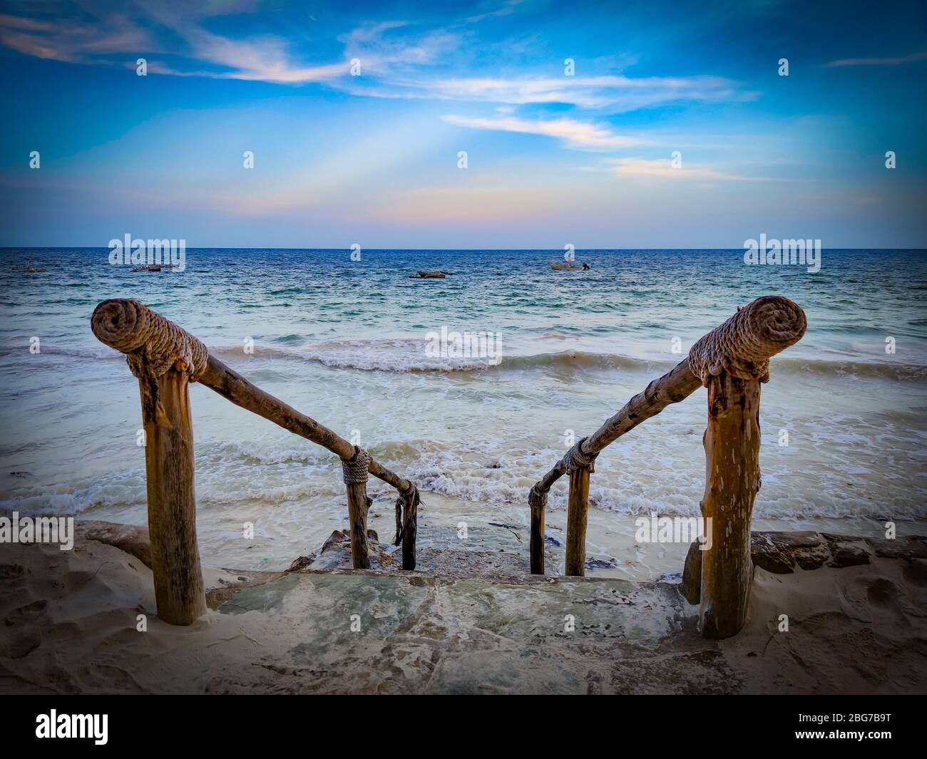 Scale in pietra al mare con ringhiera in legno. Si trova sulla spiaggia di Diani in Kenya, Africa. Onde ad alta marea raggiungono le scale. Foto Stock