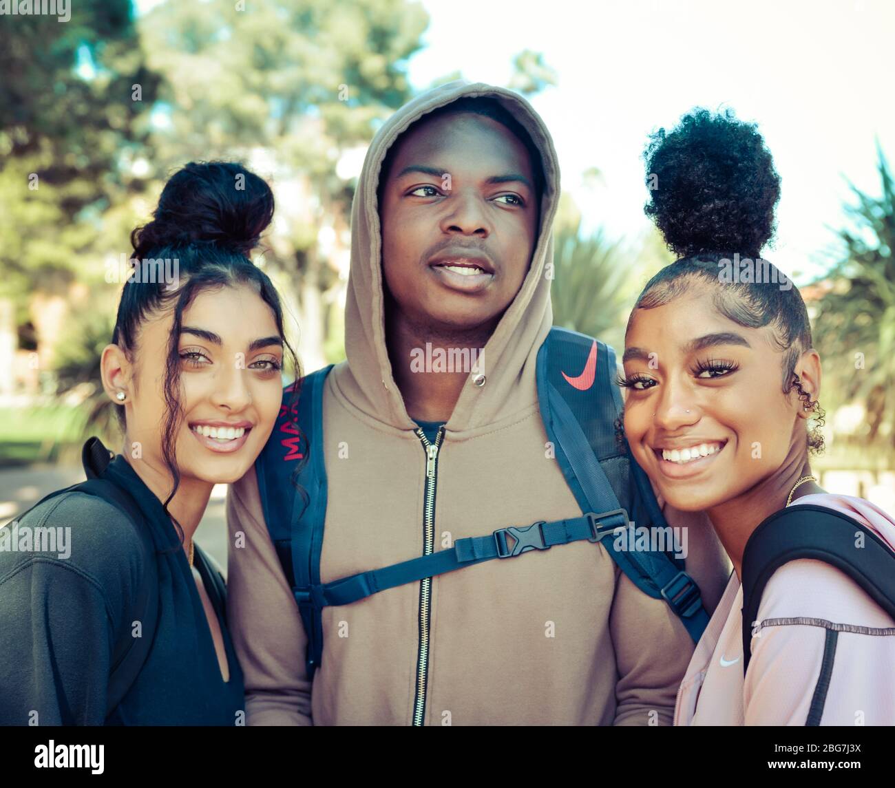 Belle giovani donne e uomo di colore, godere della vita del campus come studenti con felpa con cappuccio e tendenza updo acconciature e sorrisi in Arizona, Stati Uniti Foto Stock