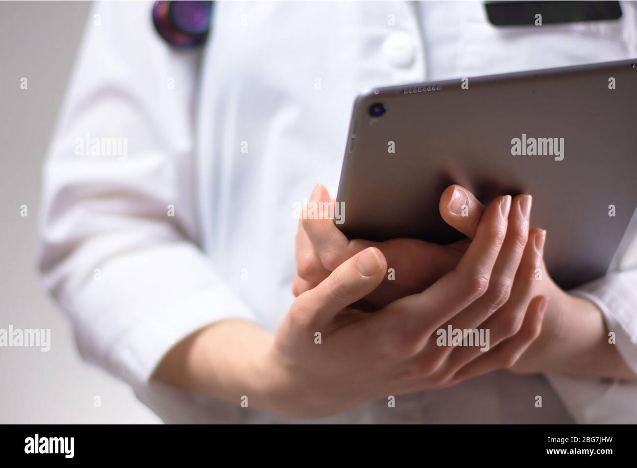 Tablet nelle mani di un operatore sanitario da vicino. Stetoscopio, stemma e stemma bianchi visibili sullo sfondo. Mani di infermiere o PA u Foto Stock