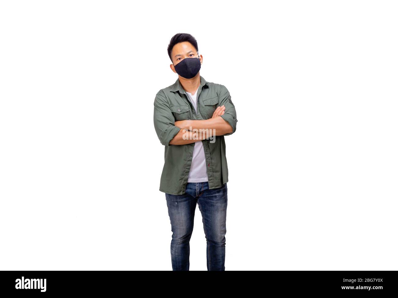 Un uomo asiatico corto di capelli in maglia di khaki e jeans che posano davanti alla macchina fotografica nell'illuminazione dello studio messa a punto mentre indossa la maschera nera Foto Stock