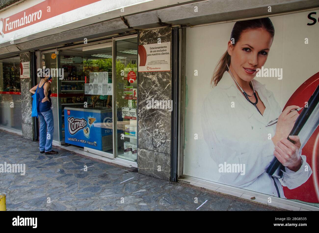 Una donna chiede prodotti in farmacia, dove la distanza sociale è marcata sul pavimento per evitare contagio Foto Stock