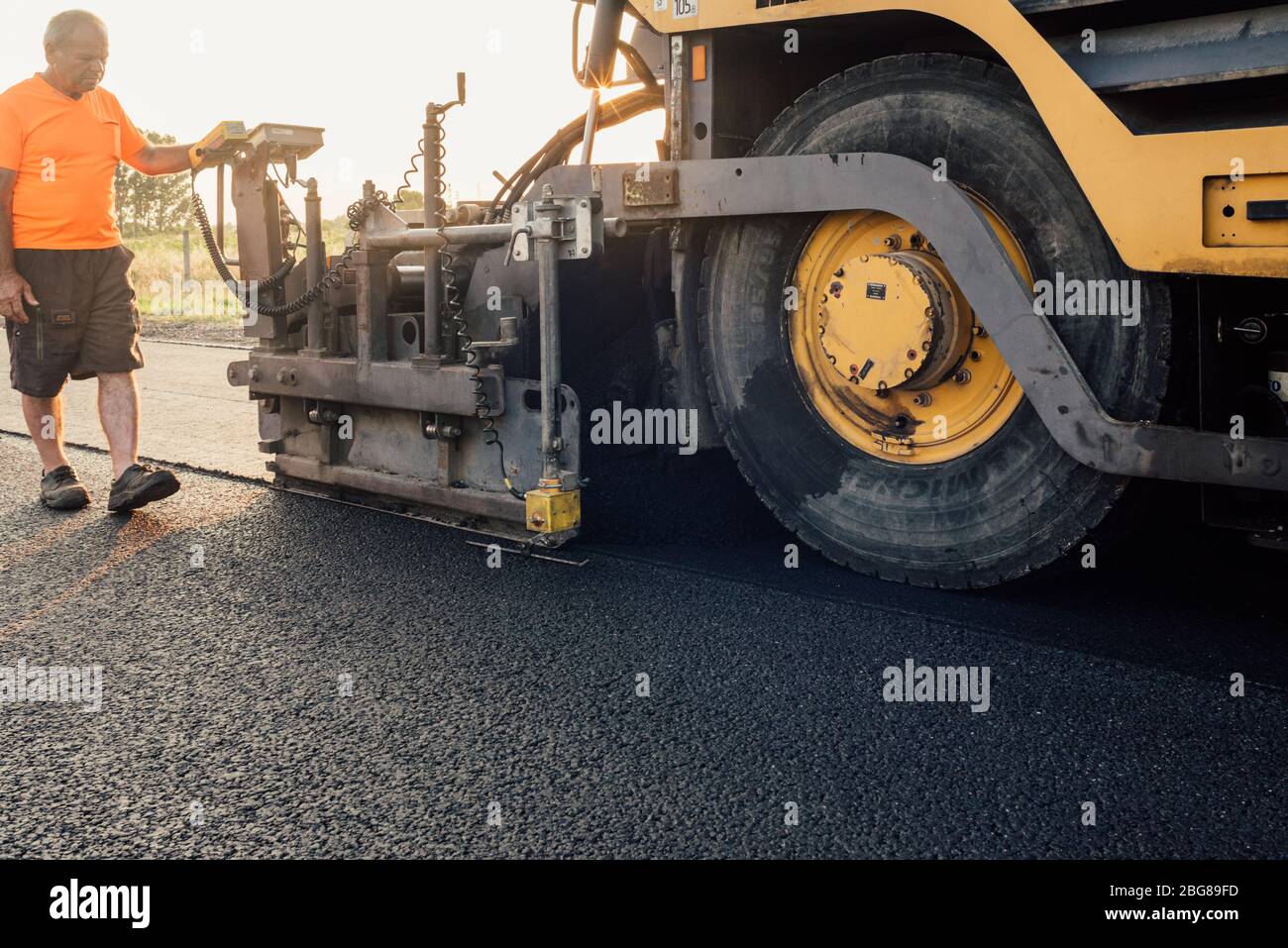 Lavoratore della strada che opera su asfaltatrice che stendono nuovo asfalto o bitume durante la costruzione di autostrade Foto Stock