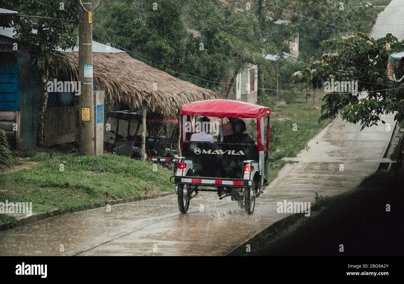 Persone che viaggiano in tuk tuk sotto la pioggia nel villaggio della giungla amazzonica Padre Cocha vicino Iquitos, nella regione di Loreto, Perù Foto Stock