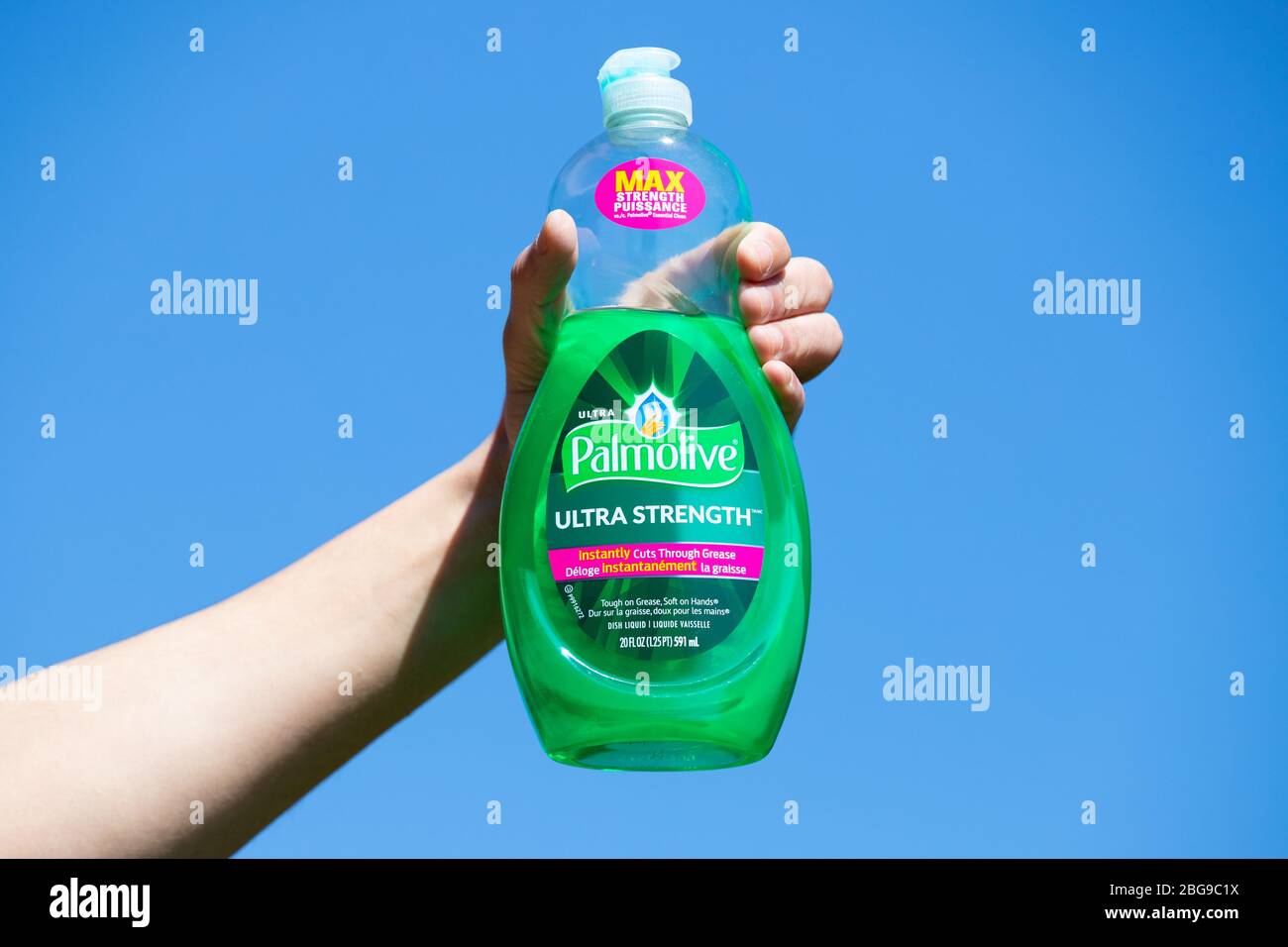 La mano contiene una bottiglia parzialmente riempita di sapone liquido per lavastoviglie Palmolive su sfondo blu. Foto Stock