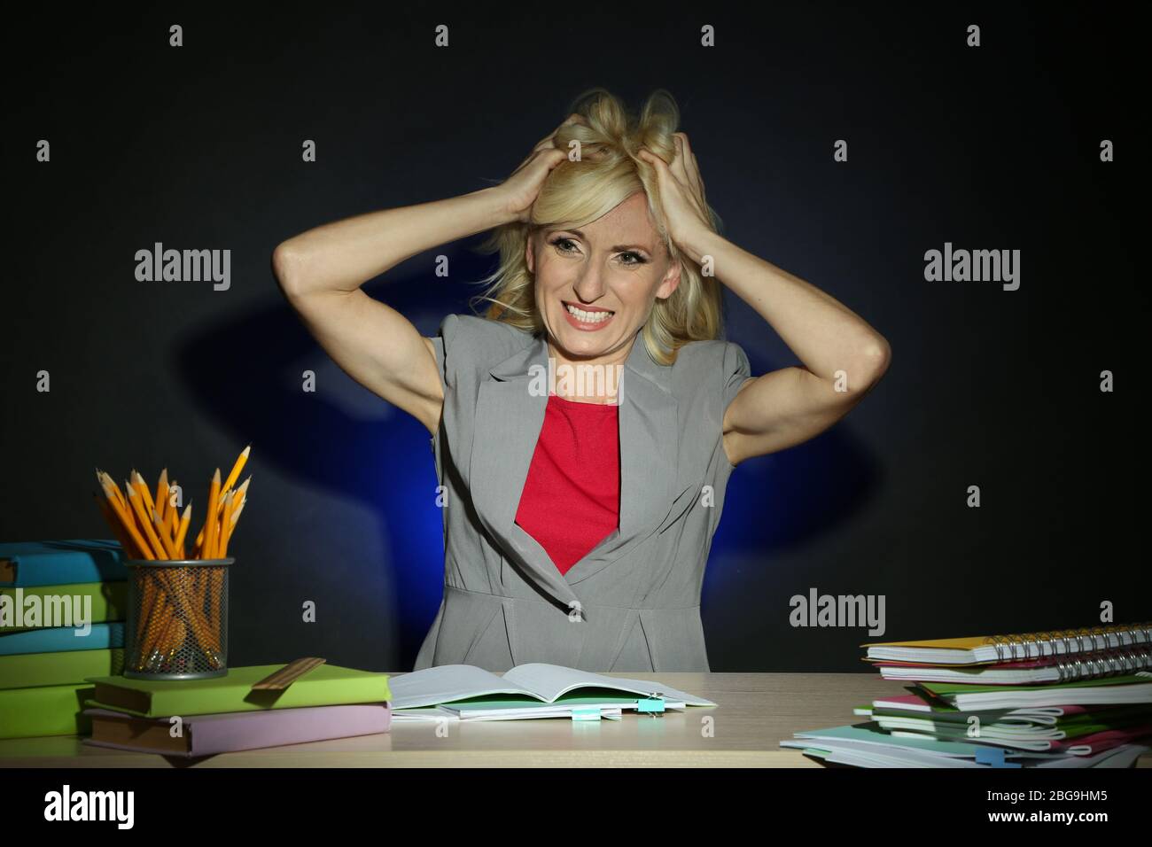 Irate l'insegnante seduto al tavolo su sfondo colorato scuro Foto Stock