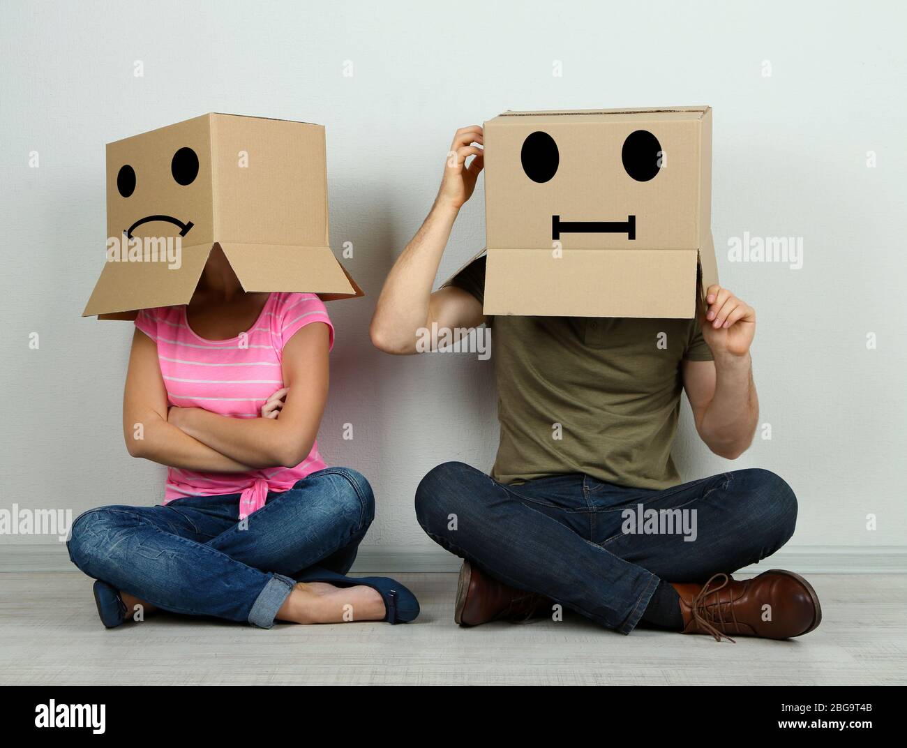 Accoppia con scatole di cartone sulle loro teste seduti sul pavimento vicino al muro Foto Stock