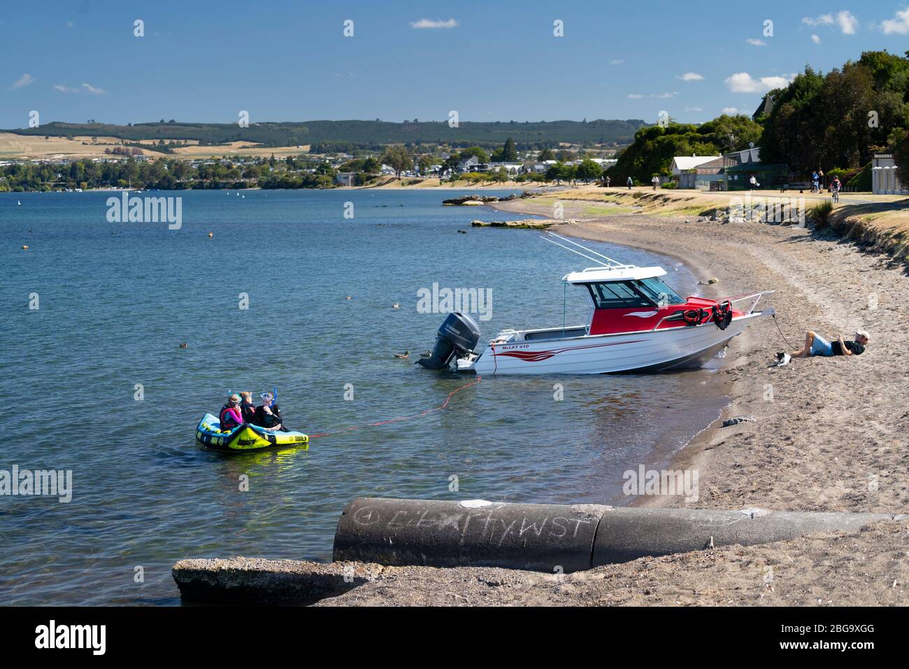 Barca sulla spiaggia e persone che si rilassano e nuotano sulle rive del Lago Taupo, Isola del Nord, Nuova Zelanda Foto Stock