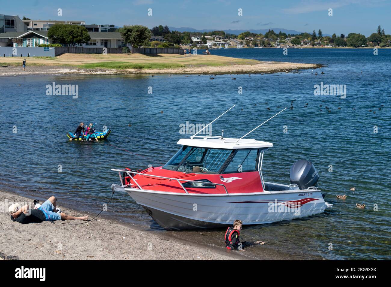 Barca sulla spiaggia e persone che si rilassano e nuotano sulle rive del Lago Taupo, Isola del Nord, Nuova Zelanda Foto Stock
