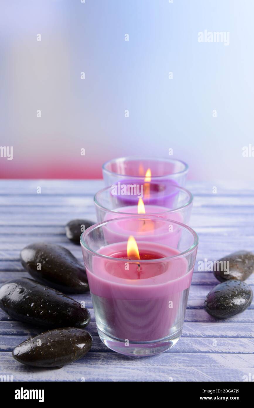 Bellissime candele colorate, pietre termali e su sfondo di legno colorato Foto Stock