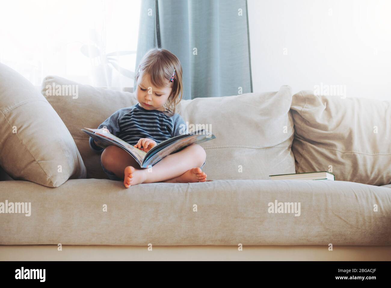 Bambina che legge un libro a casa sul divano. Formazione a distanza. Detox digitale. Foto Stock