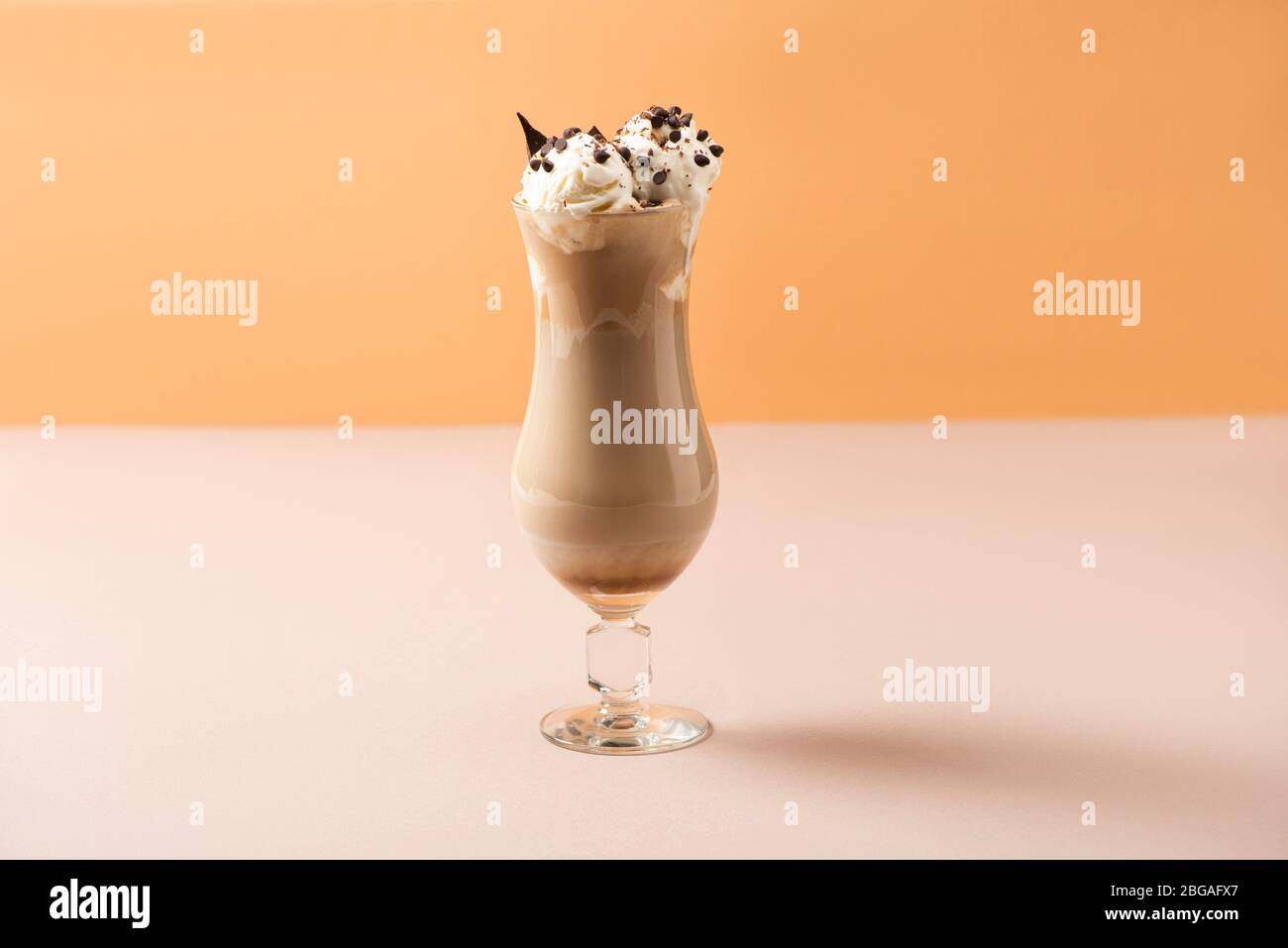 Bicchiere di milkshake con gelato e bocconcini di cioccolato su beige e arancio Foto Stock