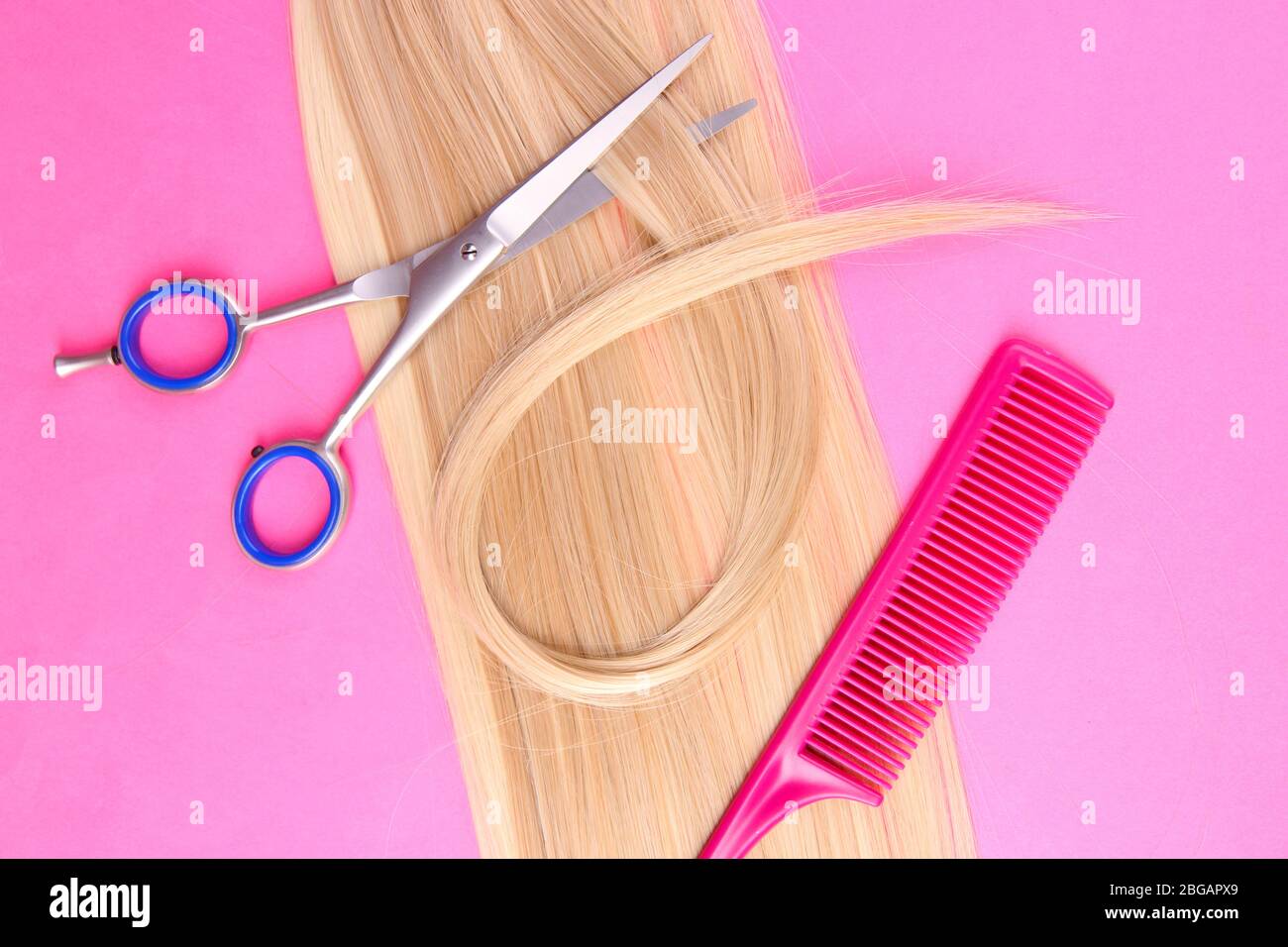 Capelli biondi lunghi con pettine e forbici su sfondo rosa Foto Stock