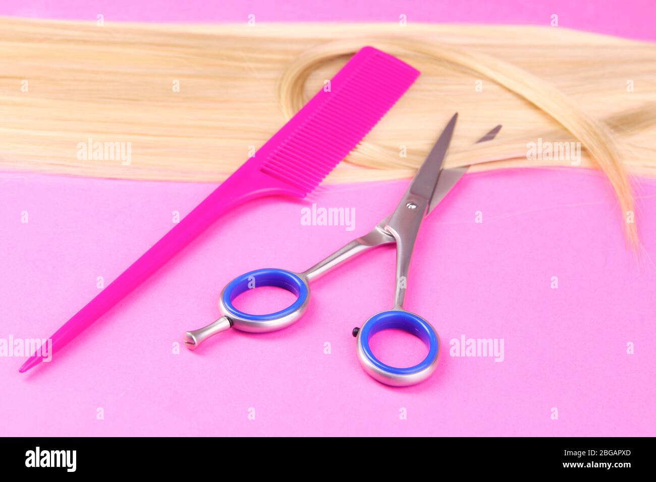 Capelli biondi lunghi con pettine e forbici su sfondo rosa Foto Stock
