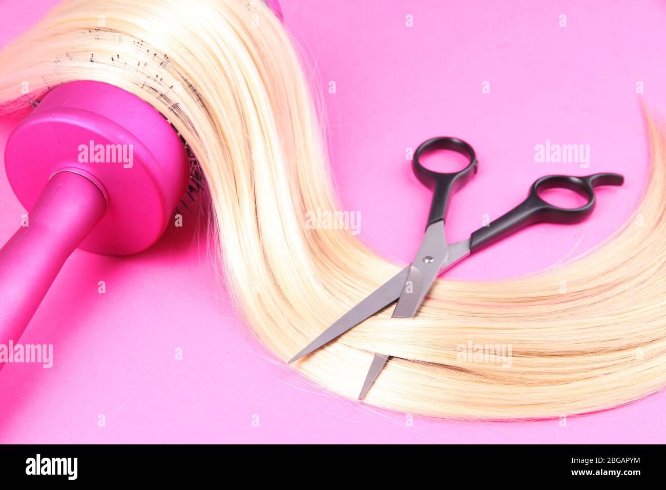 Capelli lunghi biondi con spazzola e forbici su fondo rosa Foto Stock