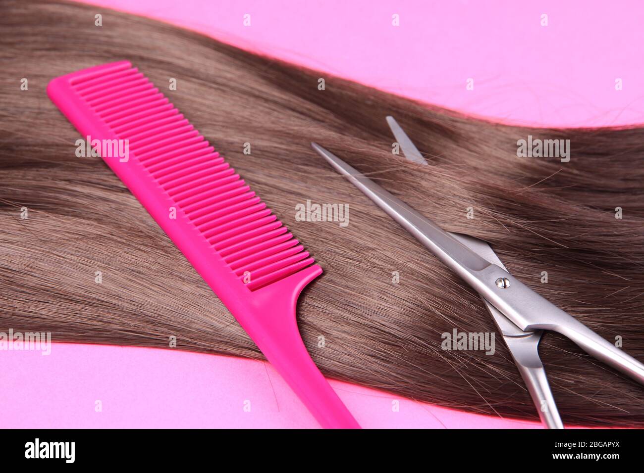 Capelli lunghi marroni con pettine e forbici su sfondo rosa Foto Stock