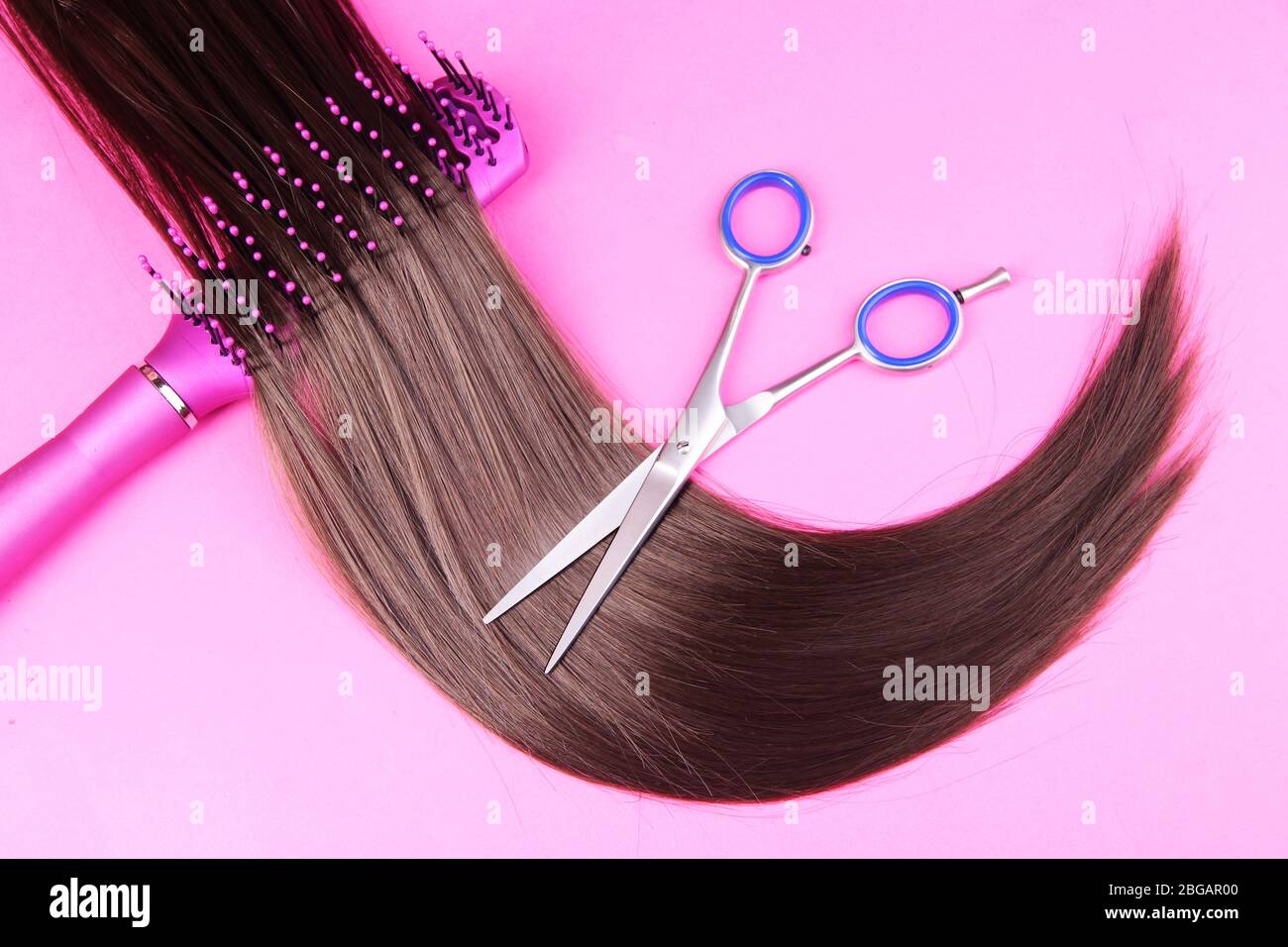 Capelli lunghi marroni con spazzola e forbici su sfondo rosa Foto Stock