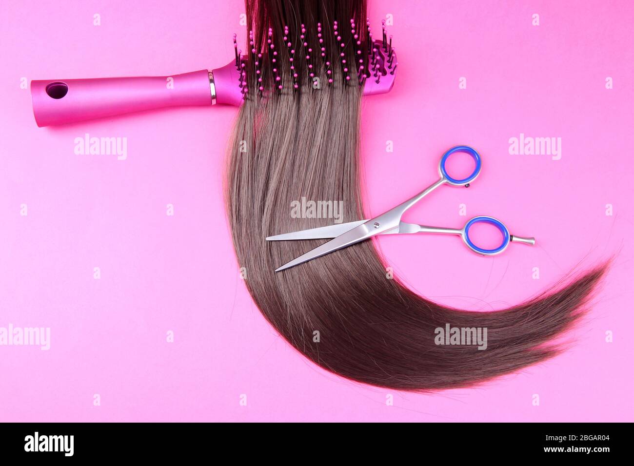 Capelli lunghi marroni con spazzola e forbici su sfondo rosa Foto Stock