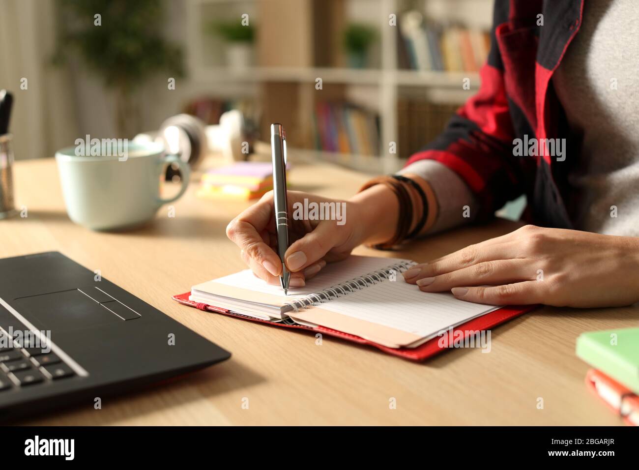 Primo piano della mano della ragazza studente che scrive su un ordine del giorno su una scrivania a casa di notte Foto Stock