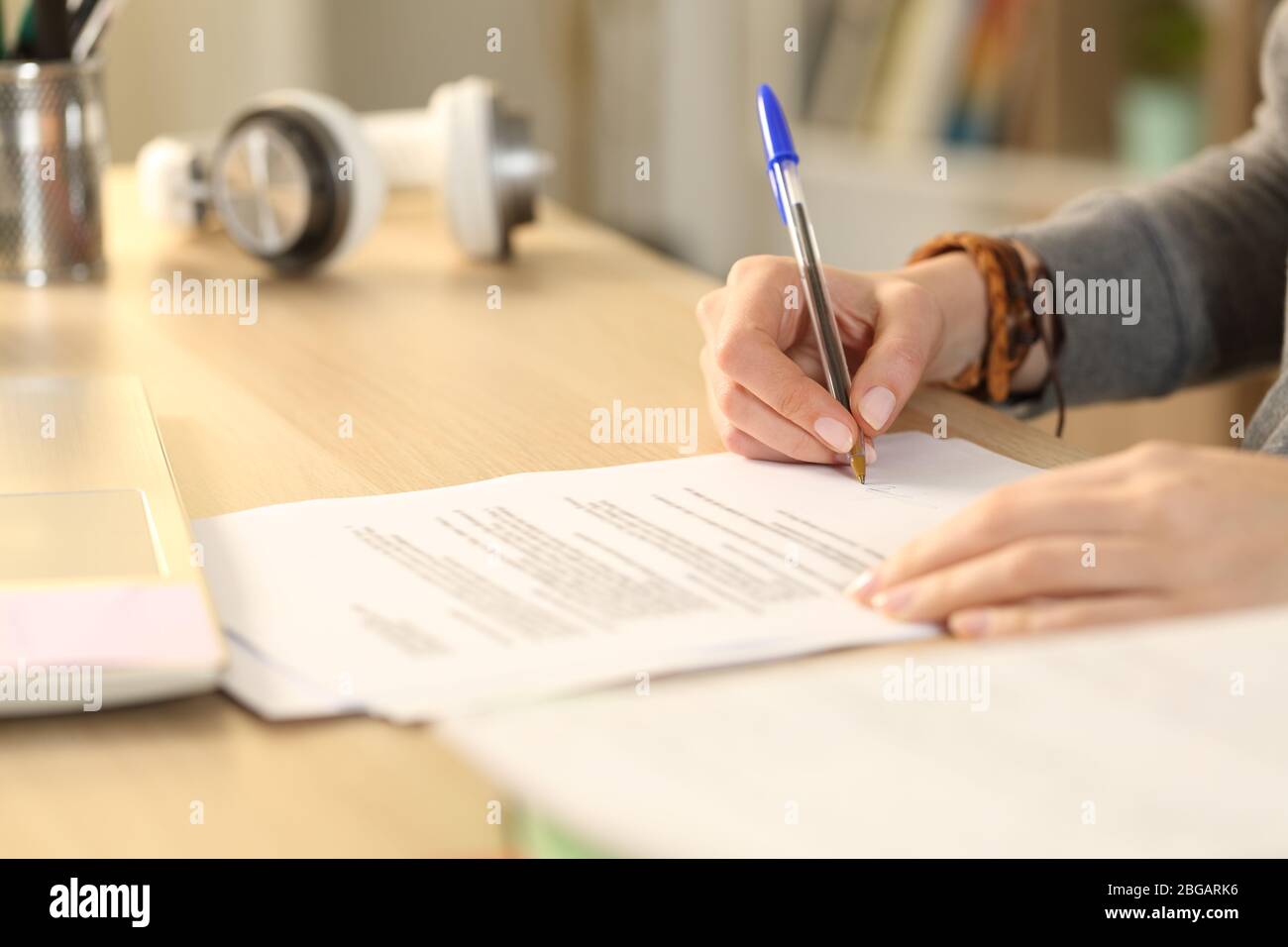 Primo piano di mani studentesca firma contratto su una scrivania a casa Foto Stock