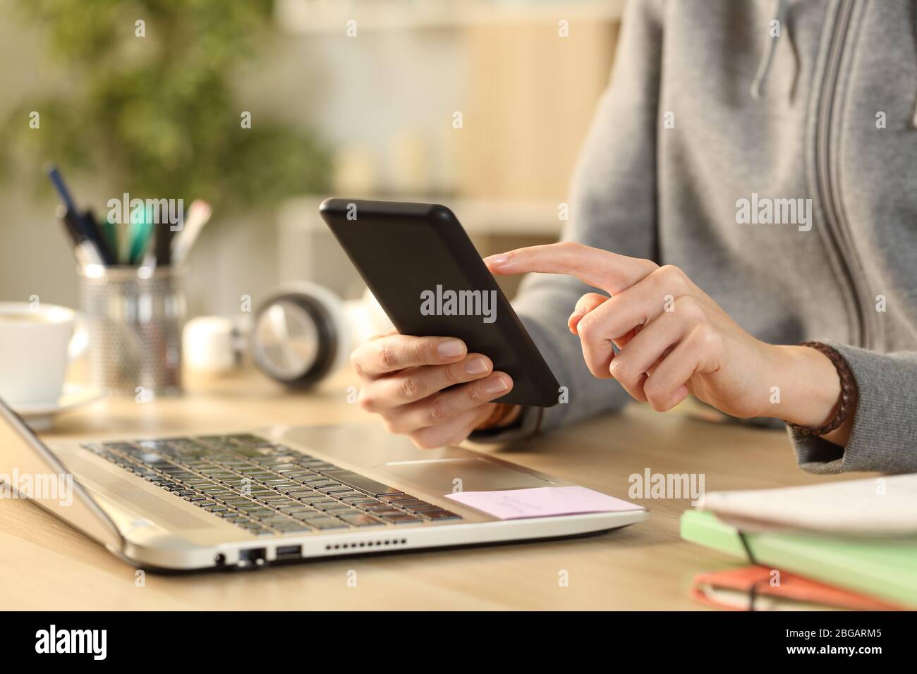 Primo piano della studentessa mani di controllo smartphone su una scrivania a casa Foto Stock