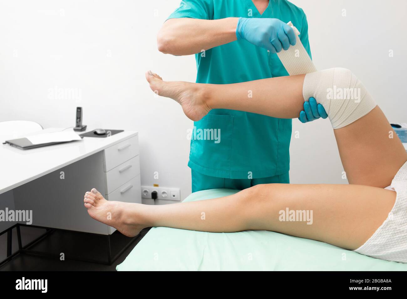 Traumatologist bending ginocchio danneggiato di una donna con un bendaggio elastico. Fisioterapista bending ginocchio primo piano Foto Stock