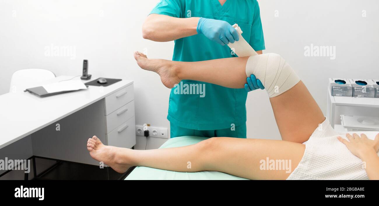 Traumatologist bending ginocchio danneggiato di una donna con un bendaggio elastico. Foto Stock