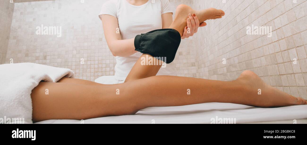 Lavoratore hammam che utilizza un guanto Kese che esegue una procedura di peeling delle gambe della donna. Peeling corpo in bagno turco tradizionale Foto Stock