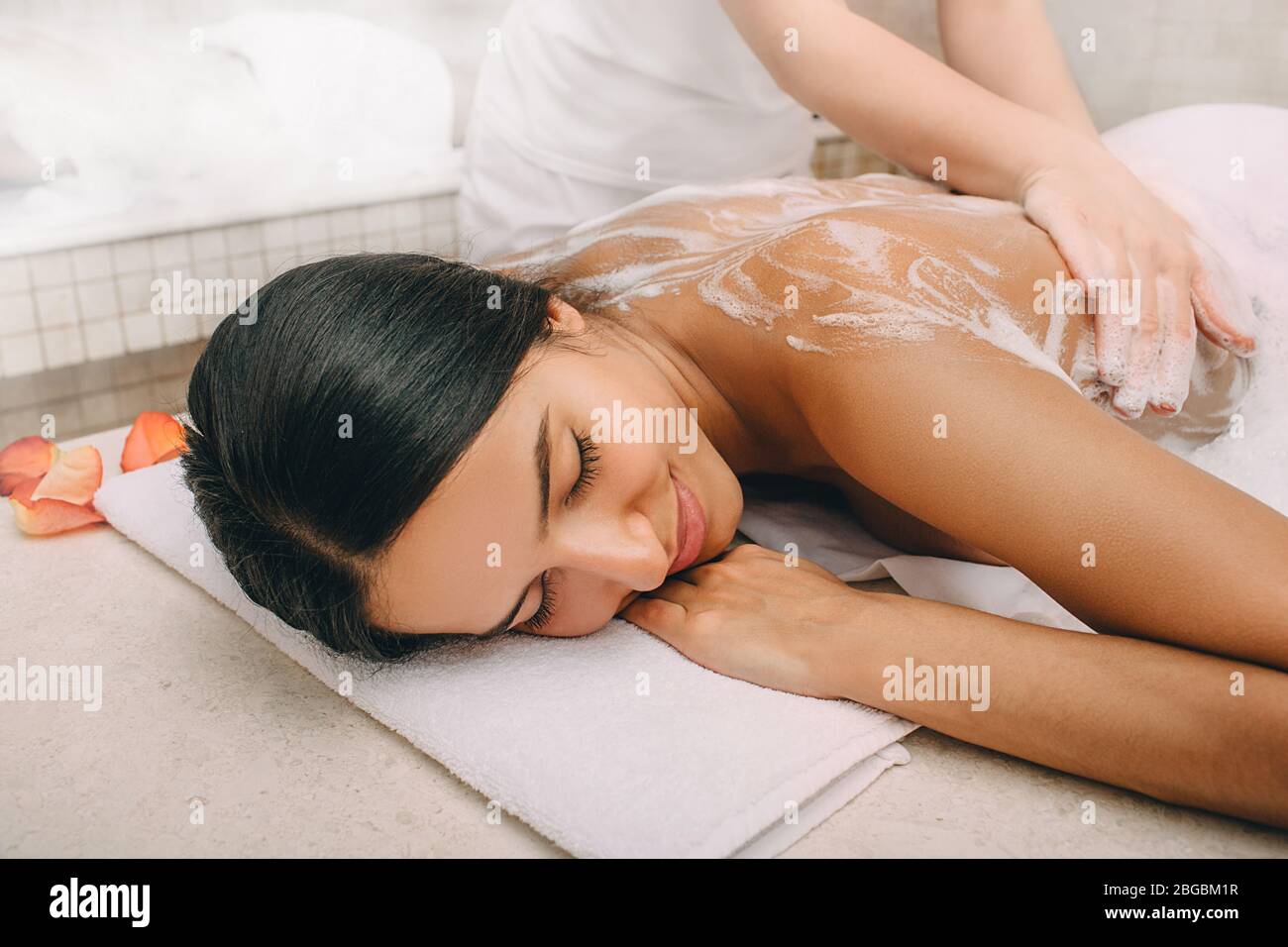 Hammam. Massaggiatore che applica la schiuma ad una donna bella sul corpo. Donna rilassata in un hammam Foto Stock