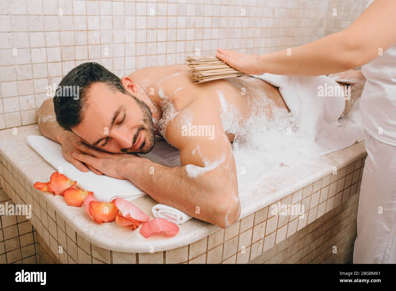 Turco che si gode massaggio con bambù in bagno turco. L'operatore dell'hammam lava la pelle degli uomini. Massaggio in schiuma Foto Stock