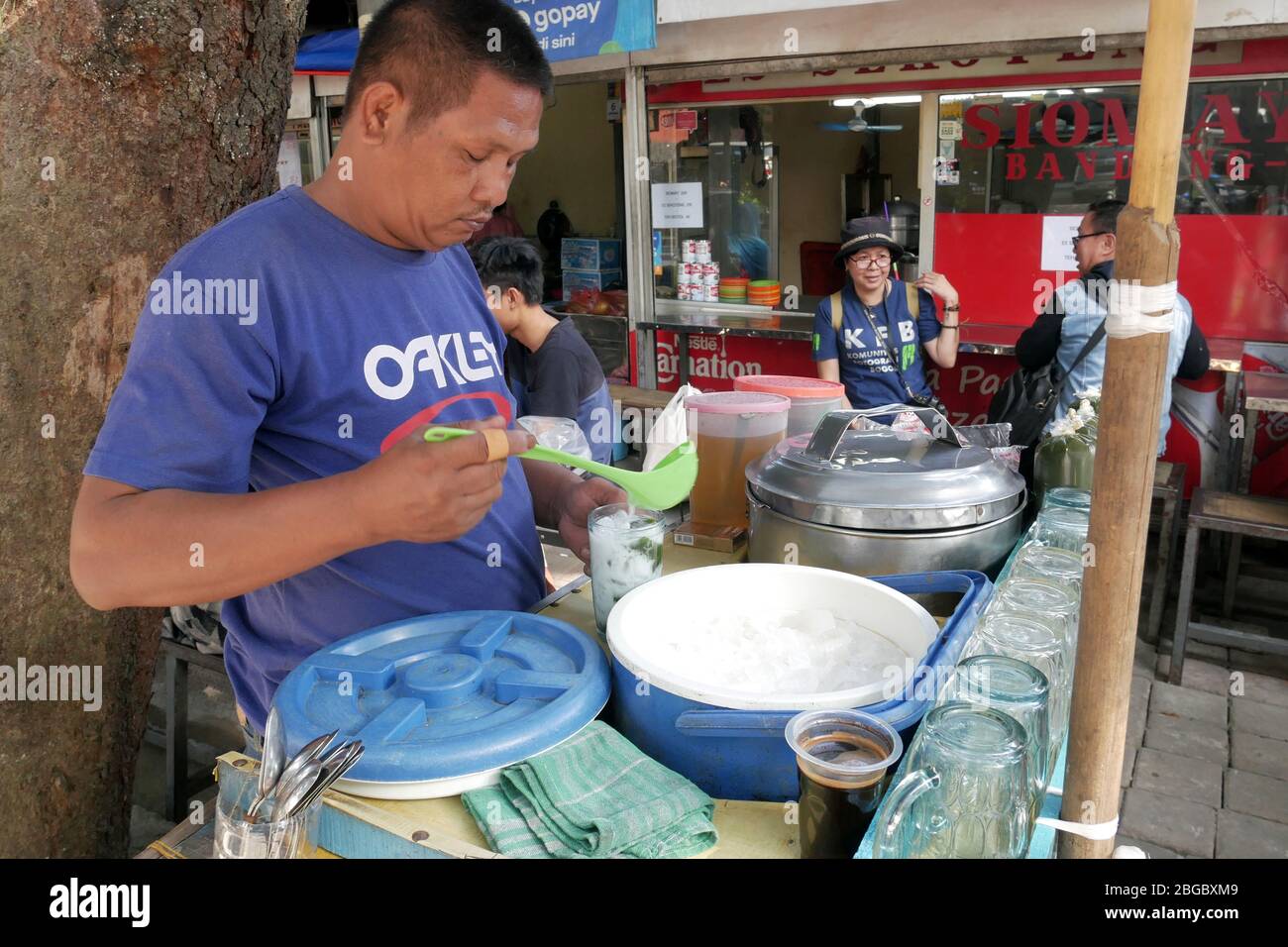 Un venditore di cibo di strada prepara un bicchiere di bevande nella sua stalla mentre il suo cliente è seduto. Foto Stock