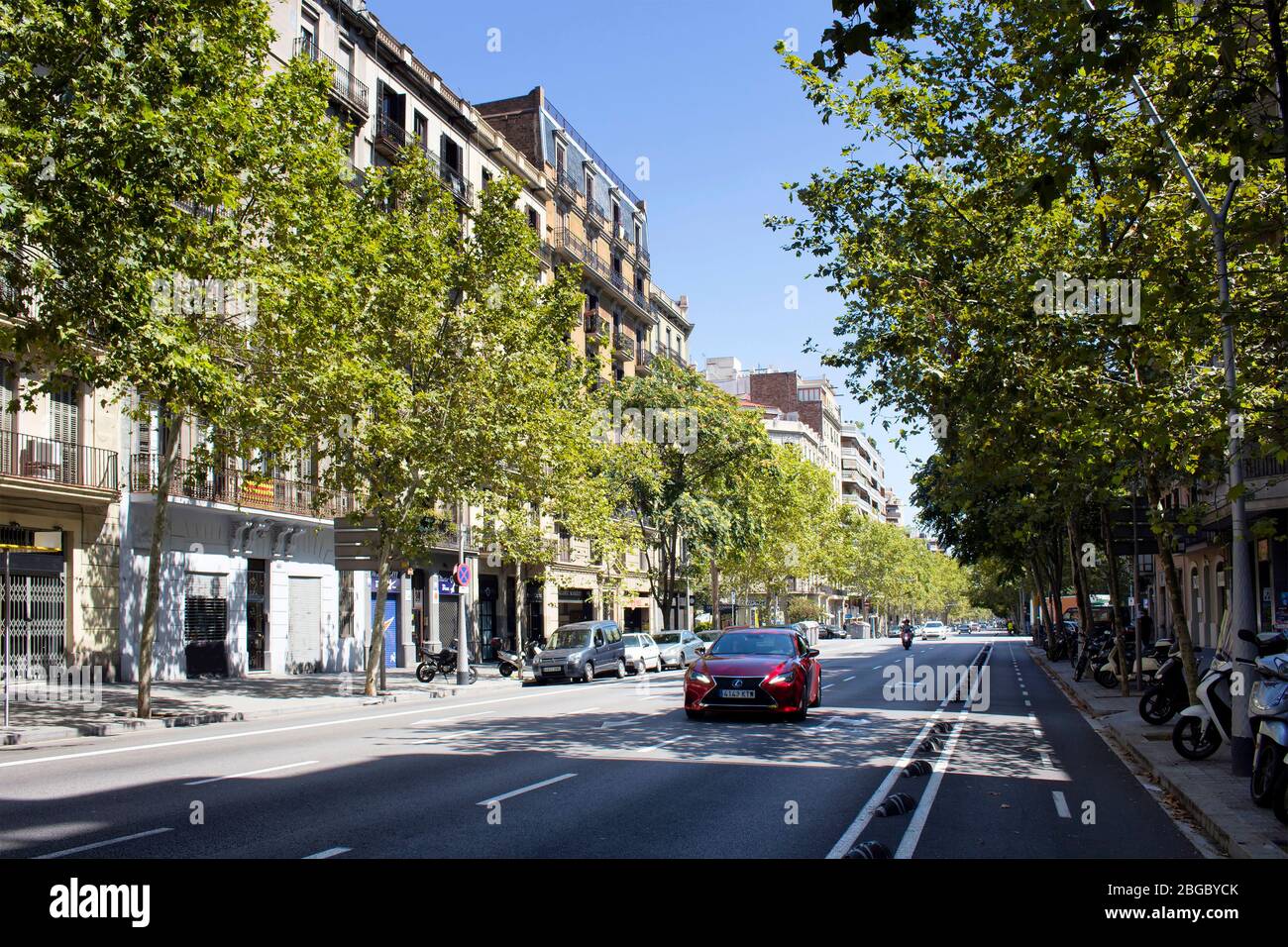 Vista di una macchina rossa sulla strada della città di Barcellona. Alberi e tradizionali, tipici edifici residenziali sono nella vista. È una giornata estiva soleggiata. Foto Stock