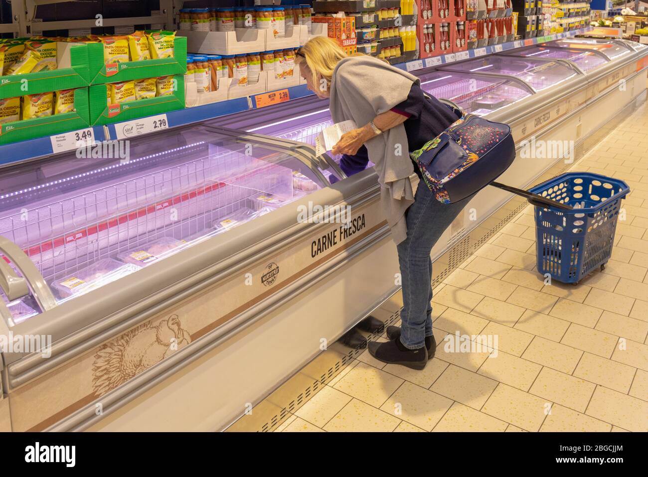 Donna con lista di shopping in mano scegliendo carne da un banco refrigerato in supermercato spagnolo. Foto Stock