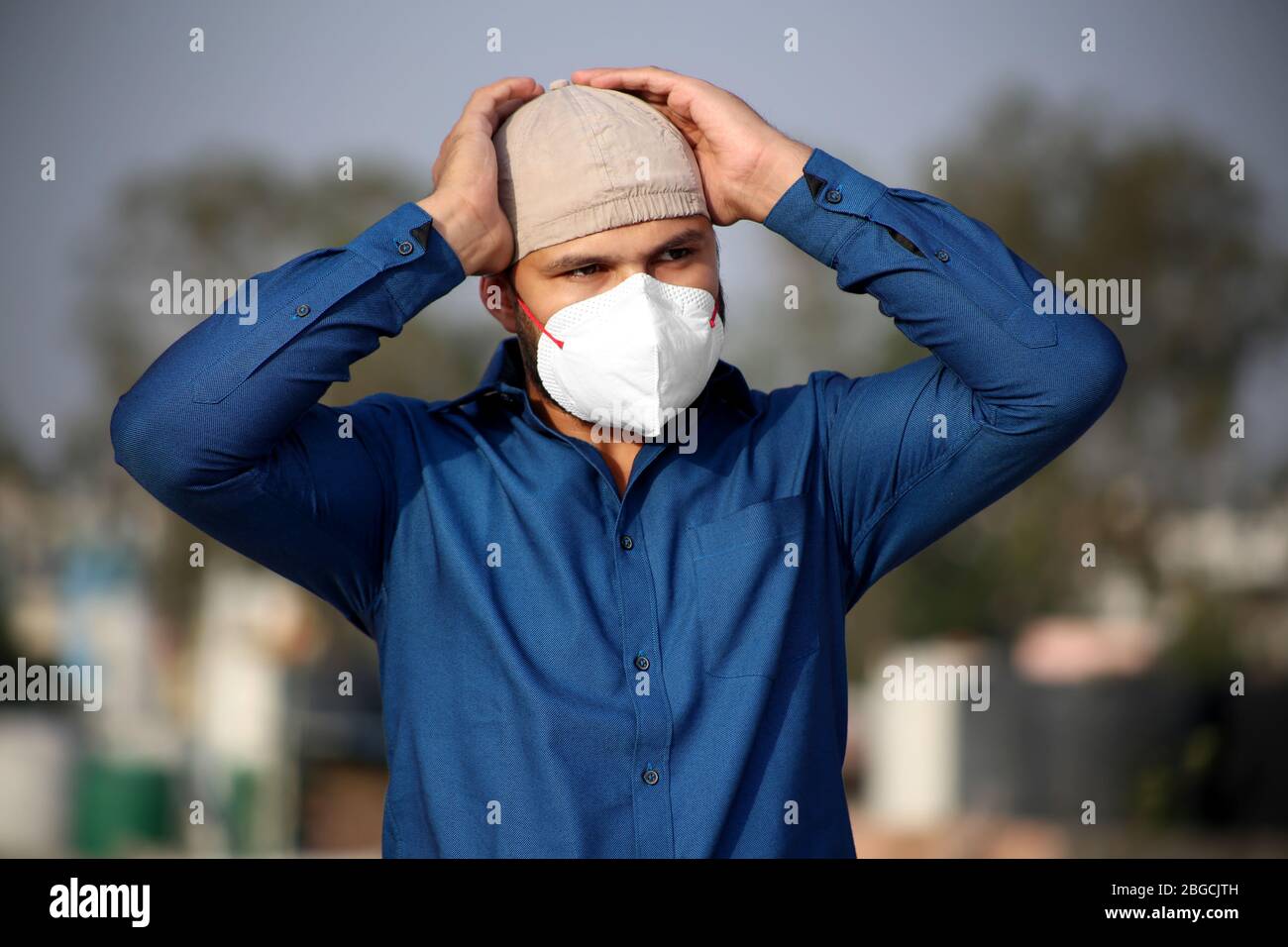 Giovani uomini di etnia indiana in piedi all'aperto e lui coprire il suo viso con maschera di inquinamento per la forma di protezione dai virus Foto Stock