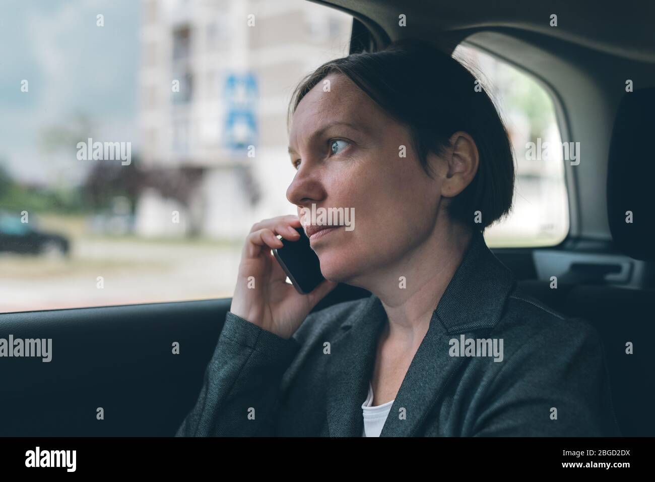 Donna d'affari delusa che parla sul telefono cellulare sul sedile posteriore dell'automobile, il concetto di affari in movimento. Elegante persona caucasica adulta con smartph Foto Stock