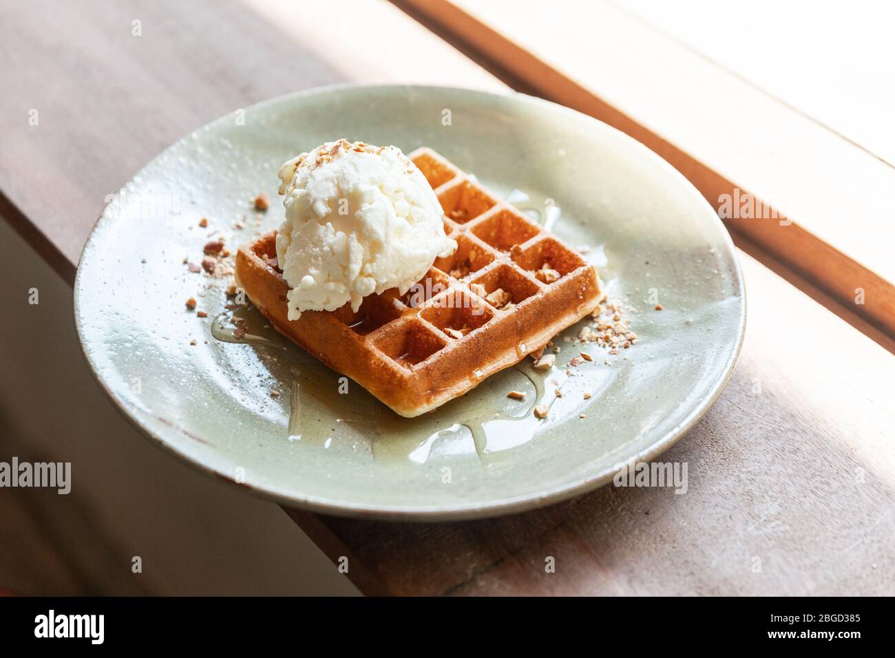 Classica aggiunta di waffle fatti in casa con un cucchiaio di gelato alla vaniglia. Guarnire con mandorla schiacciata e sciroppo d'acero. Servito in piatto di ceramica. Foto Stock