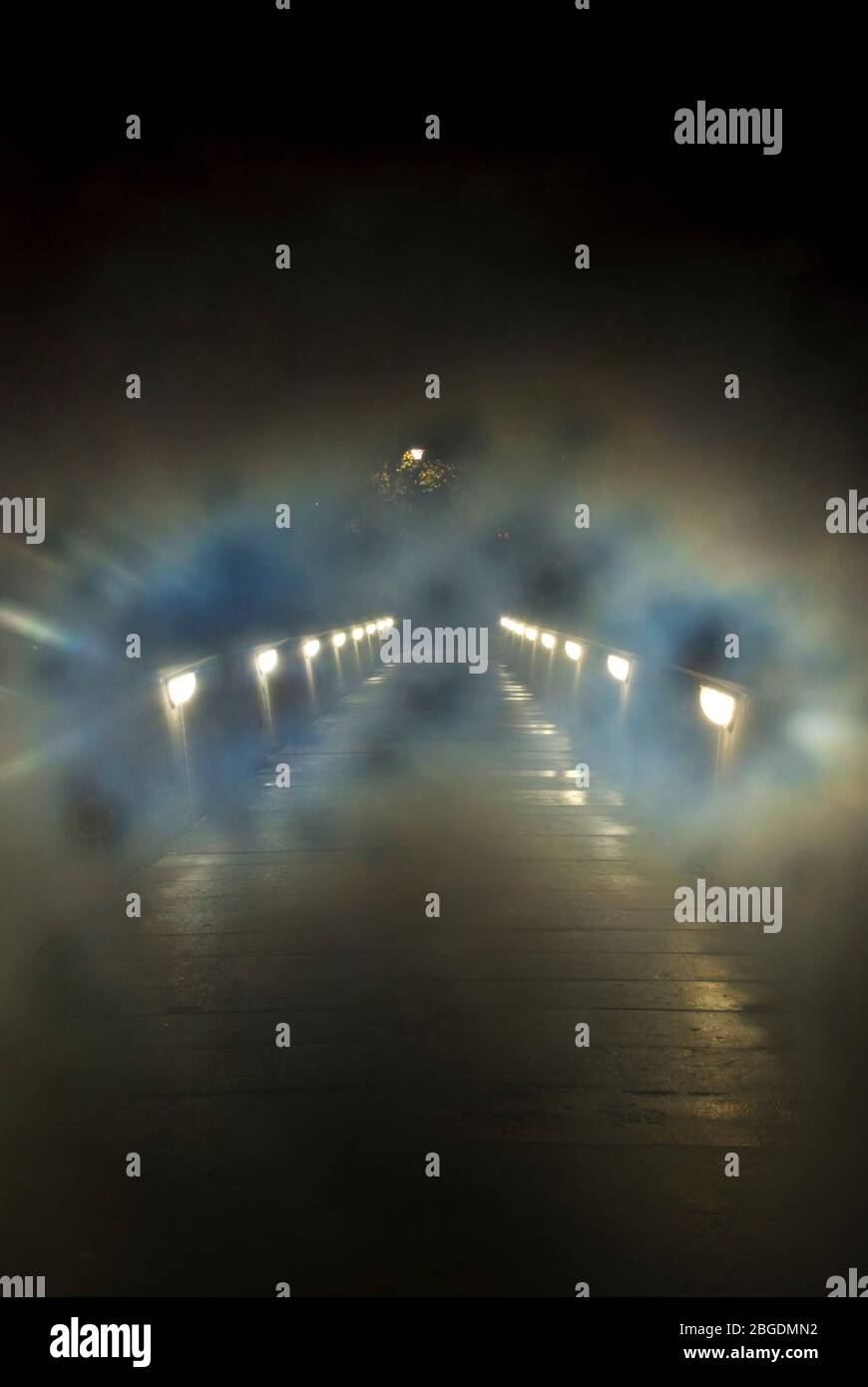 Sentiero in cemento sul ponte preso di notte in condizioni nebbie e nebbie con luci del ponte basse e riflessioni sul percorso che conduce all'oscurità Foto Stock
