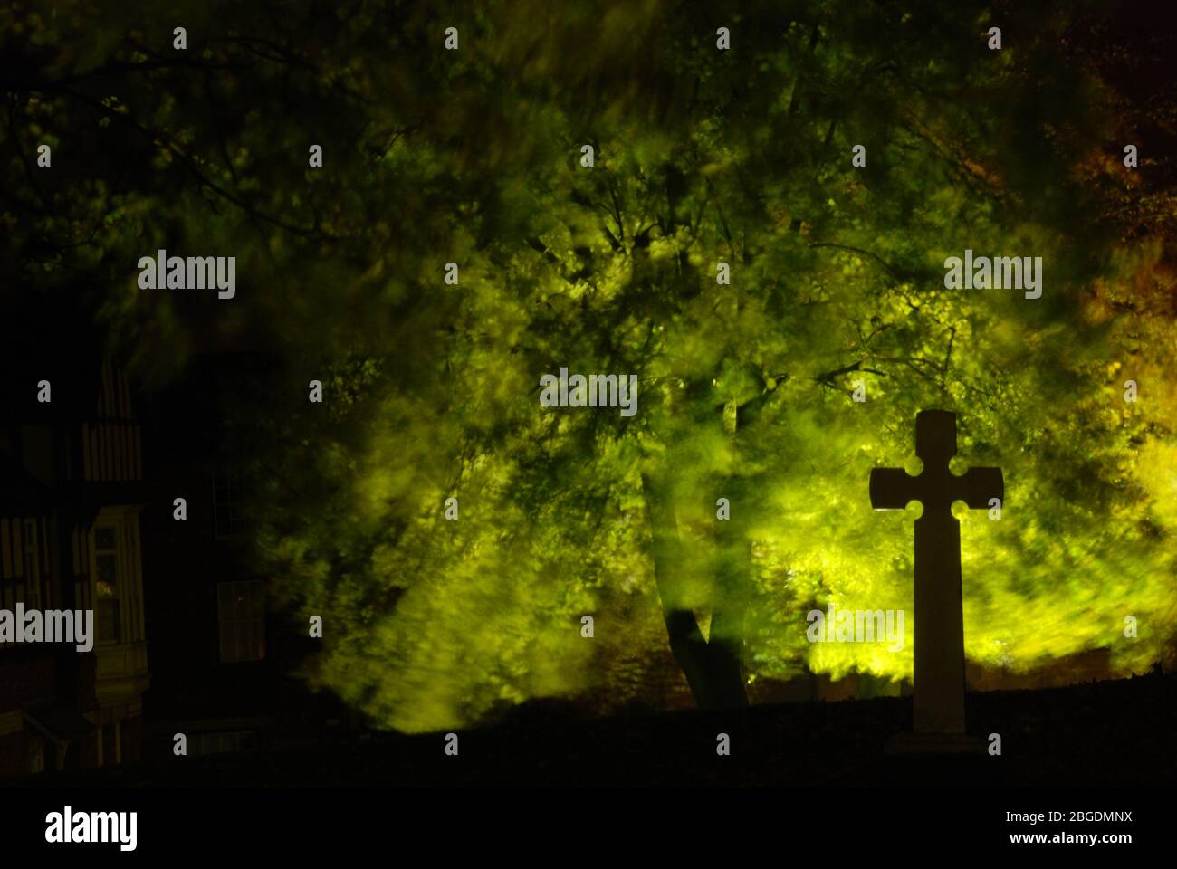 Immagine notturna della croce solitaria nella silhouette contro le foglie di albero illuminate sul retro che mostrano un movimento sfocato da una leggera brezza Foto Stock