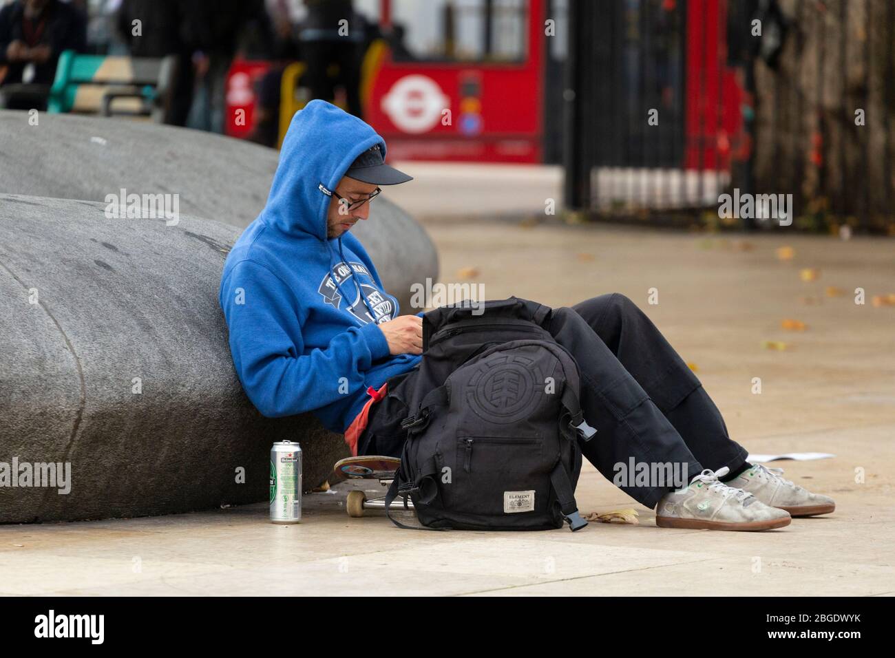 Un giovane seduto su uno skateboard e appoggiato contro una scultura a Windrush Square, Brixton, Londra Foto Stock