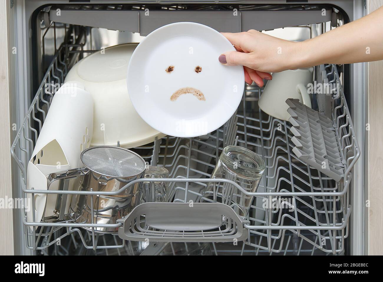 Piatti lavati male in lavastoviglie. Lavastoviglie integrata con piastre bianche davanti a vew e triste emozione su piastra. Macchina lavastoviglie rotta concetto. Foto Stock