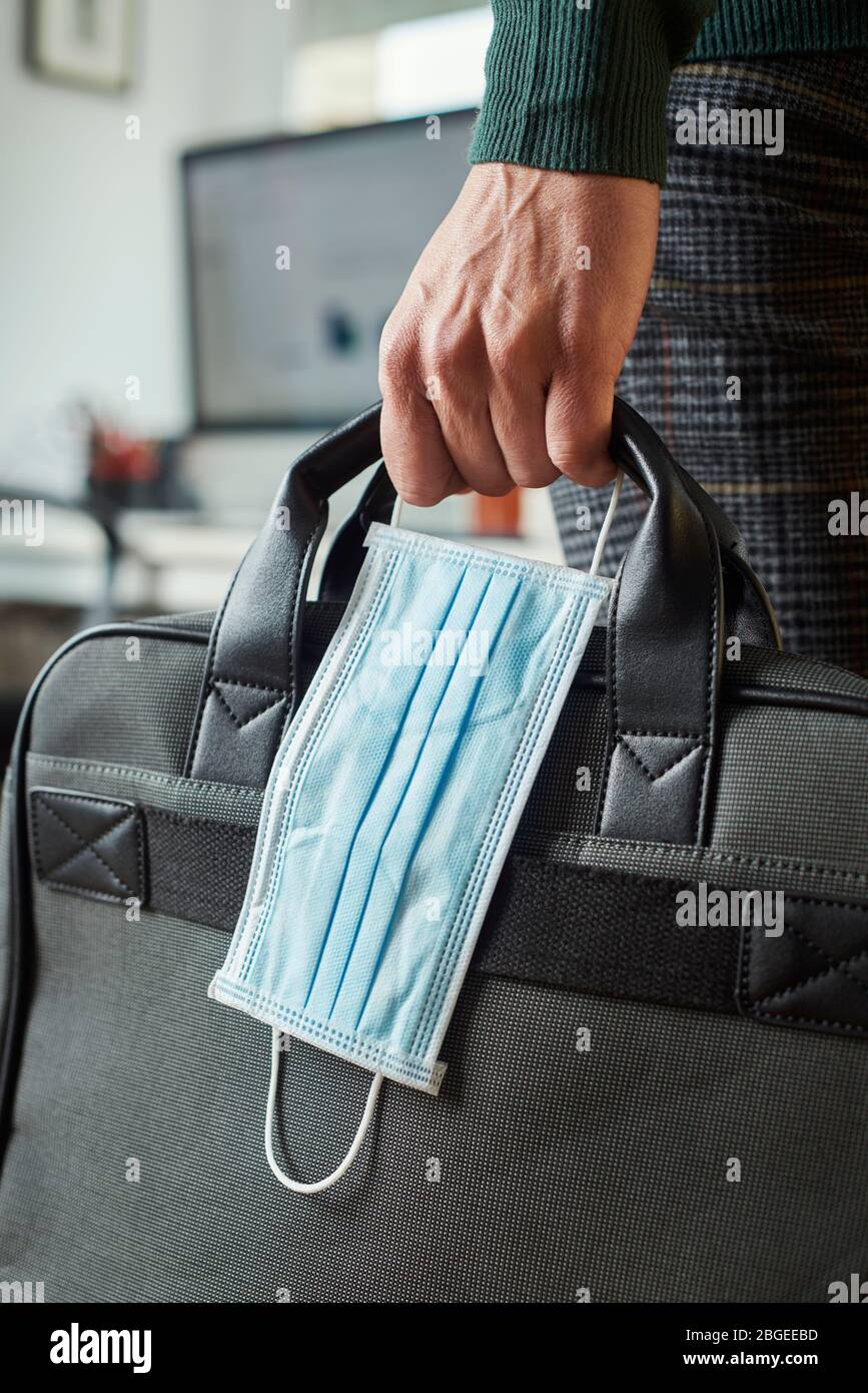 primo piano di un giovane in un ufficio che tiene in mano una valigetta e una maschera chirurgica Foto Stock